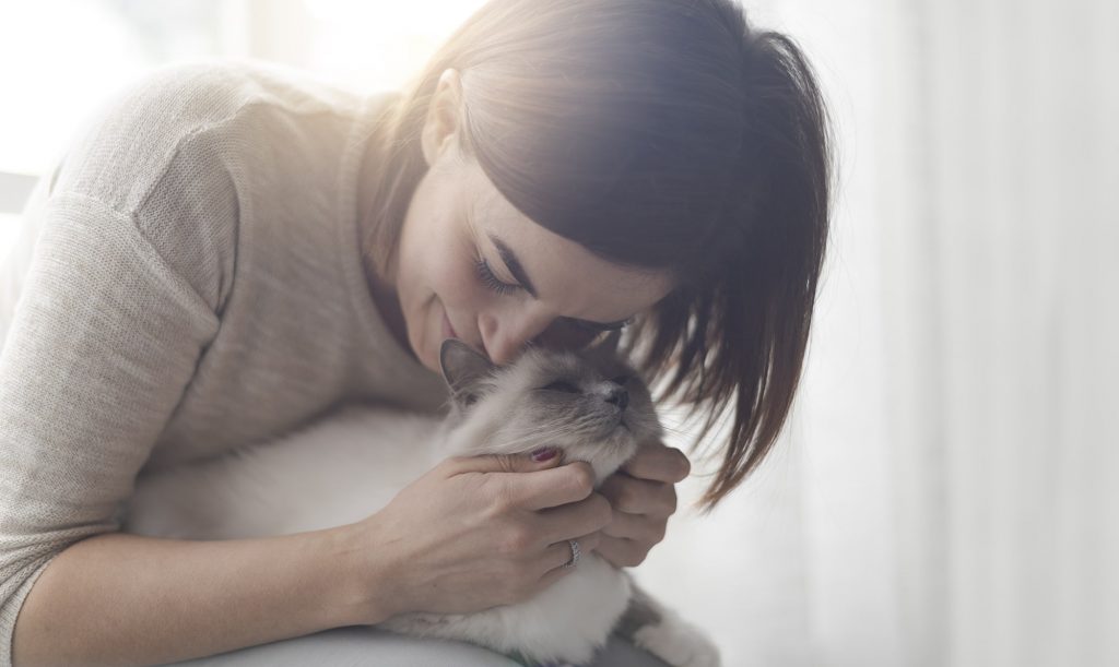 Smiling female pet owner cuddling white cat