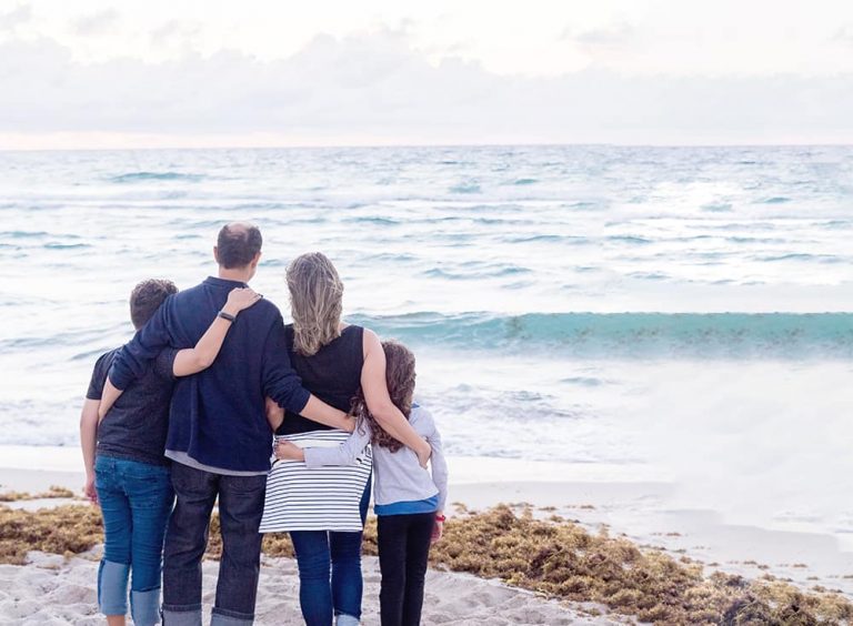 a family stands arm in arm by the beach and oceans