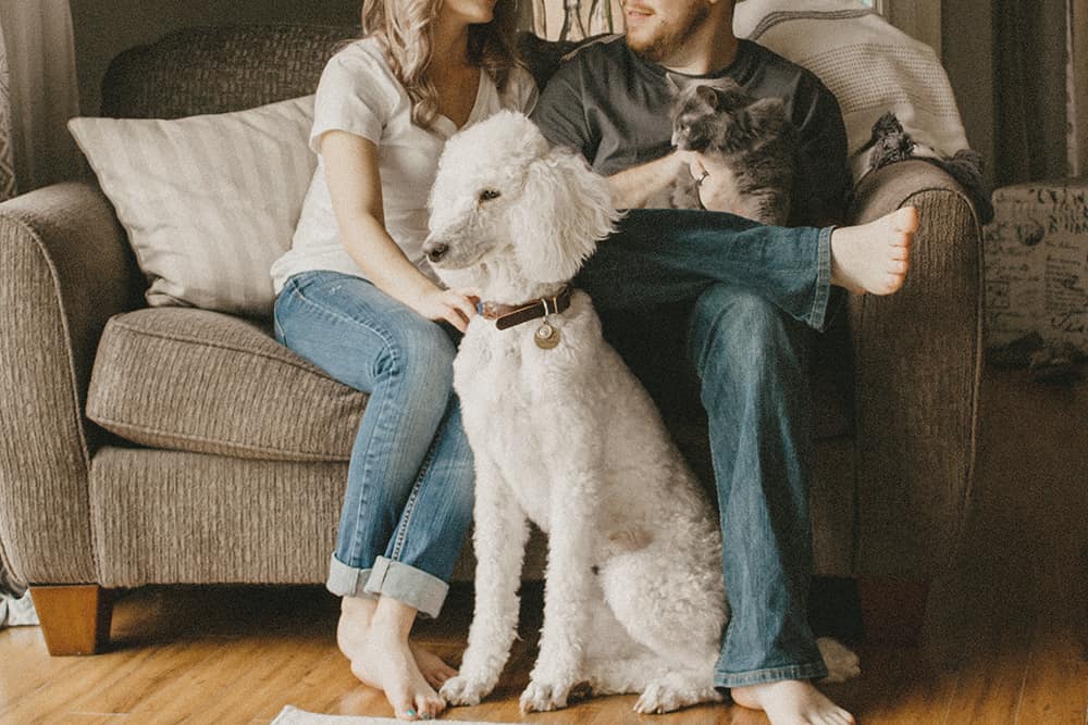 A husband and wife sitting on the couch with their pet dog